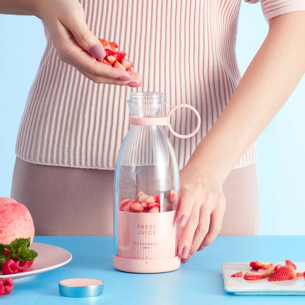 A person puts chopped strawberries into a sleek, portable light pink blender bottle with a carry loop.
