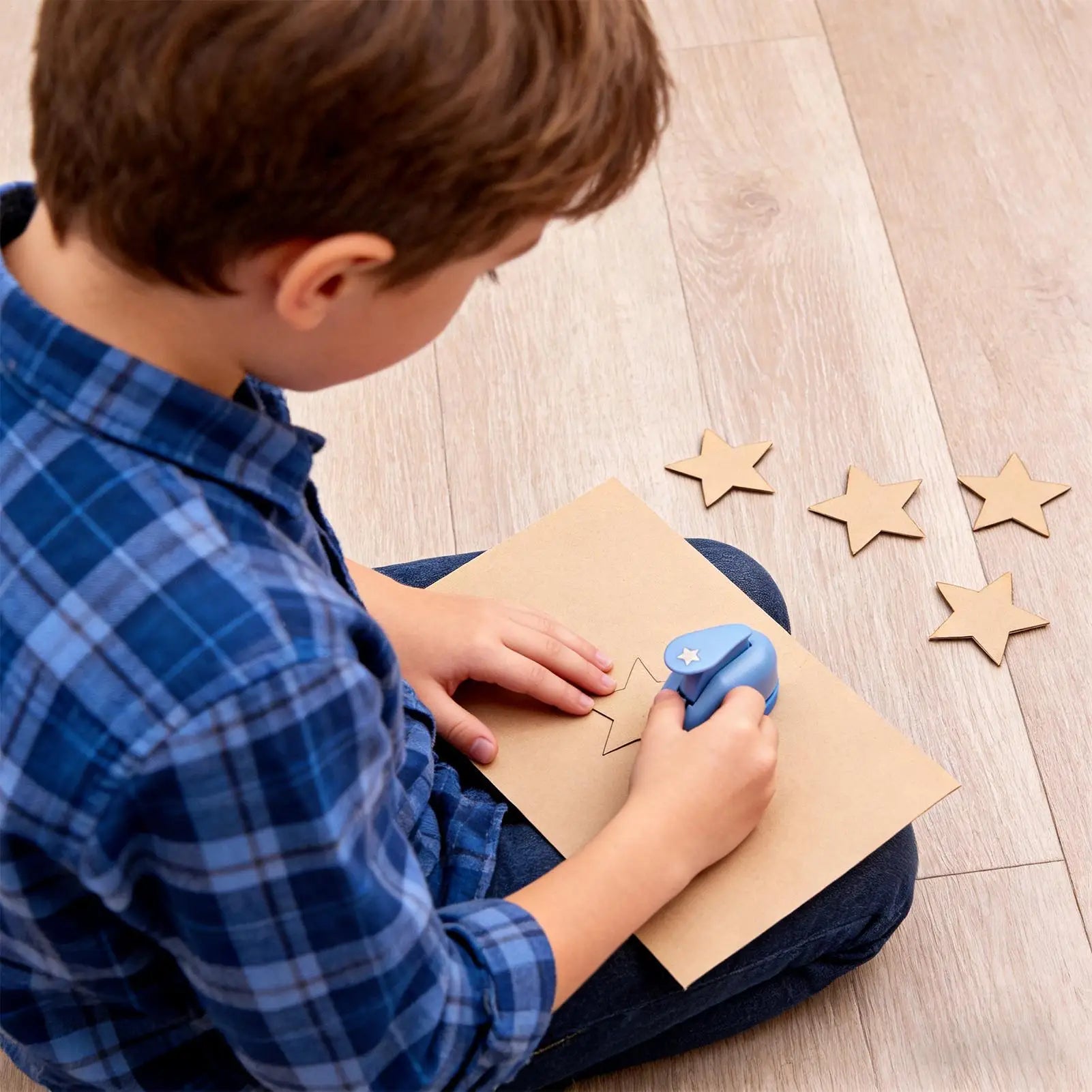 A child using a blue star-shaped paper punch to craft paper stars from a sheet of cardstock.