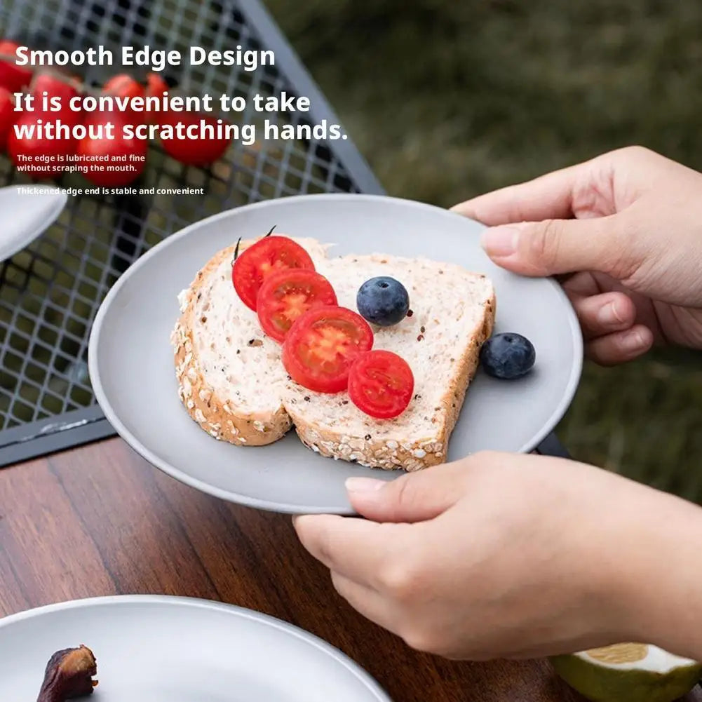 A gray round plate holds two slices of whole grain bread topped with sliced cherry tomatoes and blueberries.