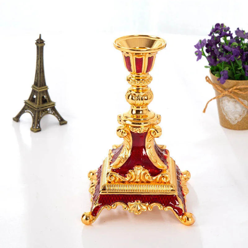 Red and gold metal candle holder with ornate scrollwork on a square base.