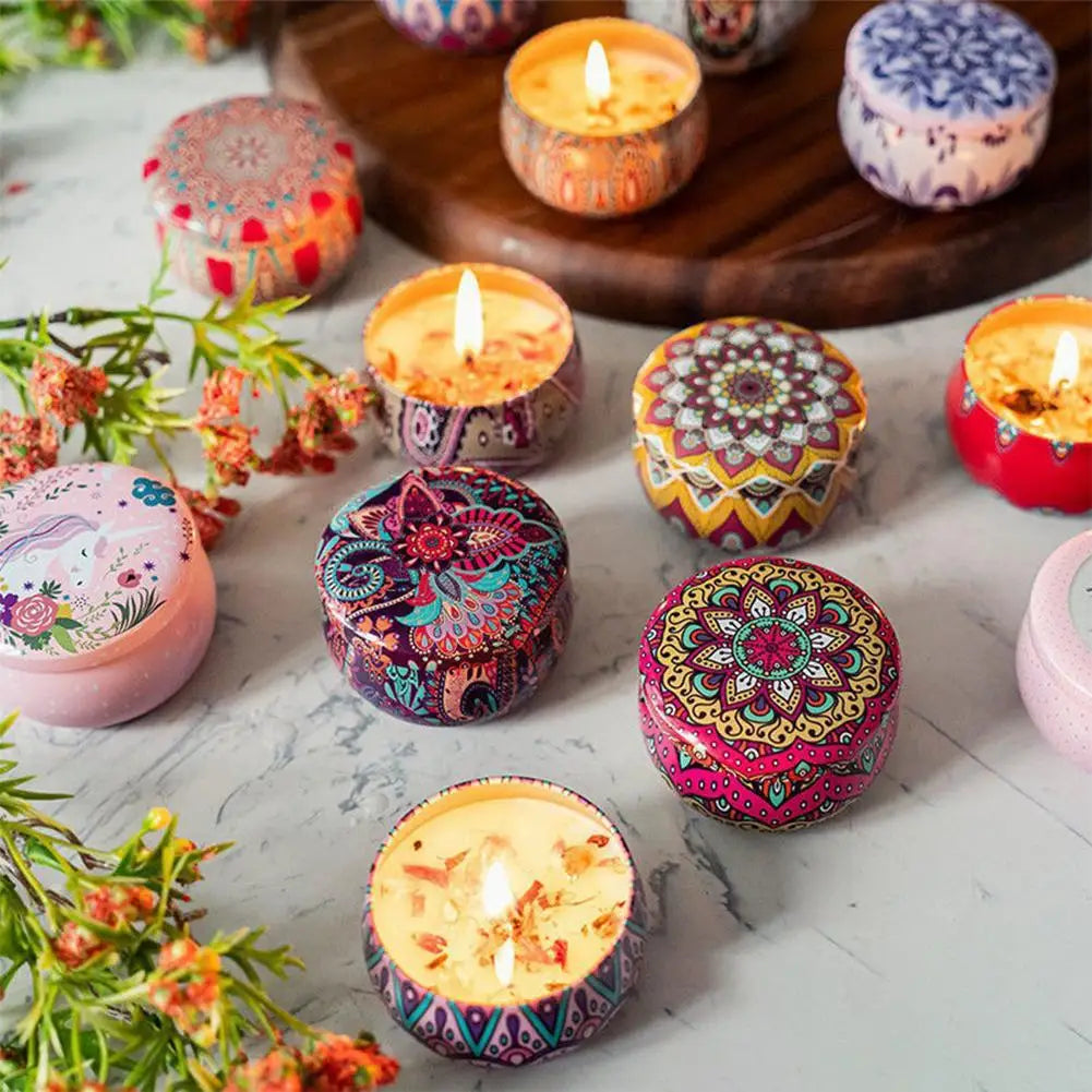 Assorted scented candles in decorative metal tins with colorful mandala and floral patterns on a marble surface.