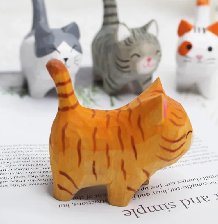Four small, hand-carved wooden cat figurines in various colours and patterns, including a featured orange tabby.