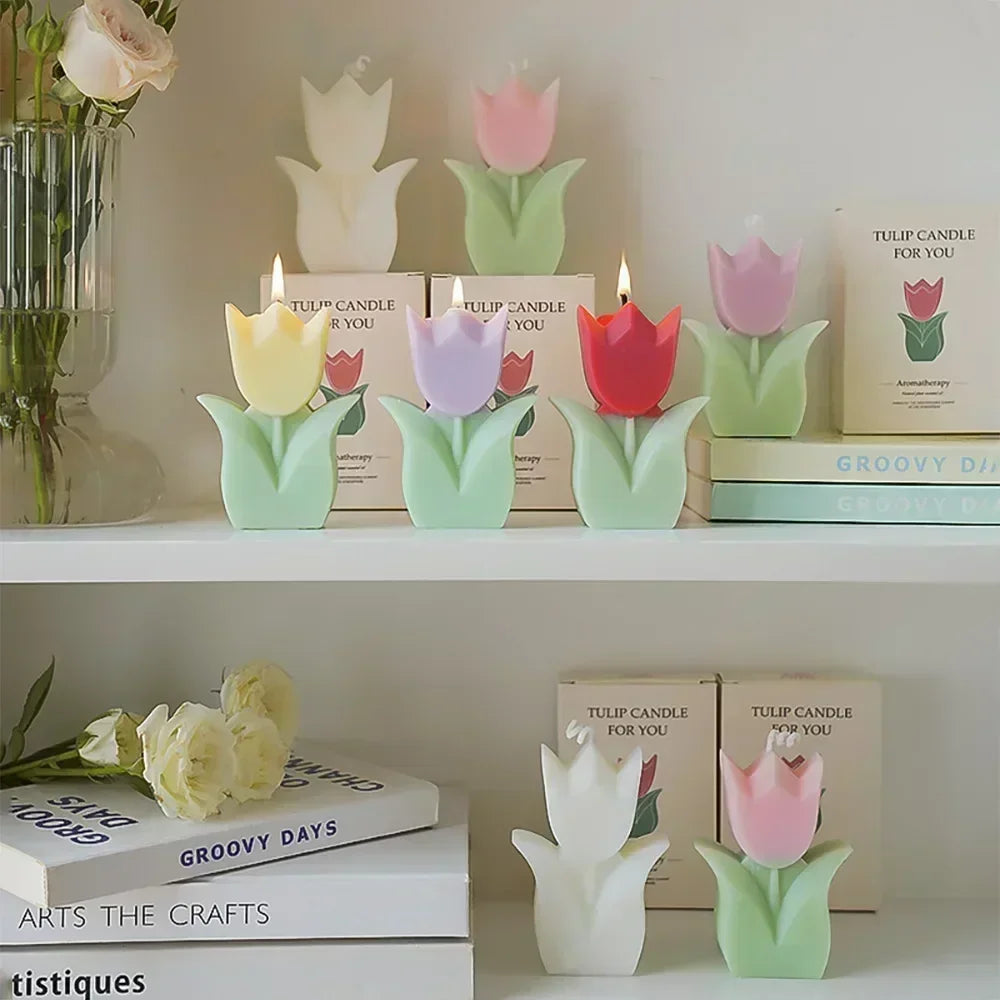 Set of colourful tulip-shaped candles in various pastel shades, some lit, displayed on a shelf with decorative books.