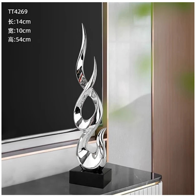 A tall, abstract silver resin sculpture with a flame-like, fluid design, mounted on a sleek black rectangular base.