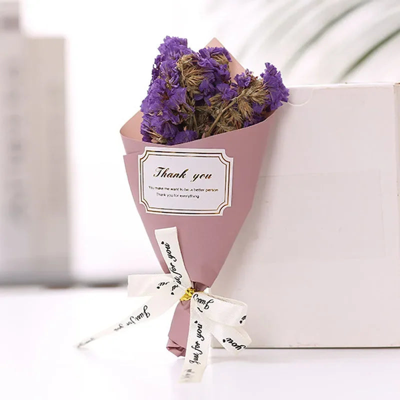 Small bouquet of purple dried flowers wrapped in pink paper with a 'Thank you' label and white ribbon.