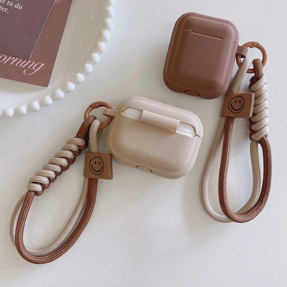 Two brown and beige silicone AirPods cases with matching braided wrist straps featuring a smiley face charm.