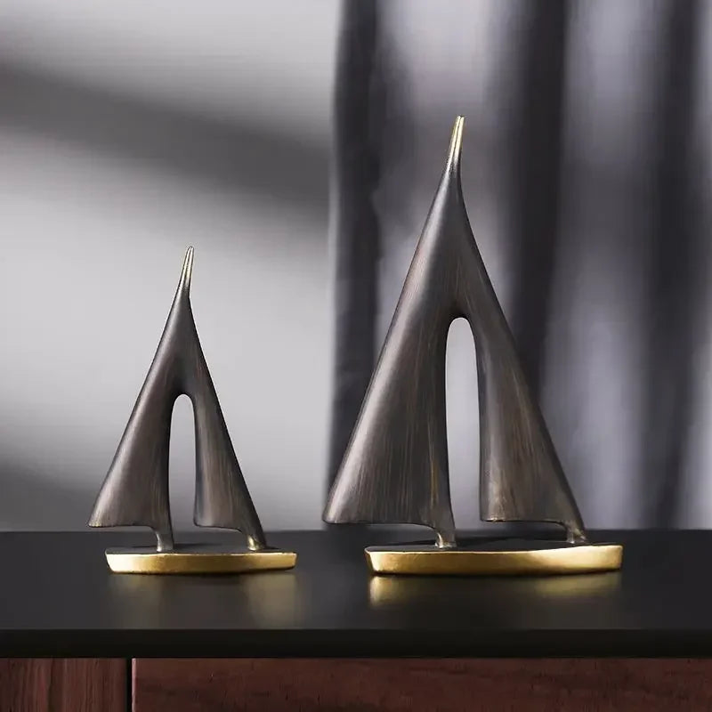 Two modern, abstract resin sailboat ornaments in bronze-effect finish with sleek, metallic gold-coloured bases.