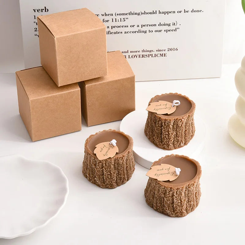 Three brown, tree-stump-shaped candles with leaf-shaped tags, alongside three plain brown kraft gift boxes.