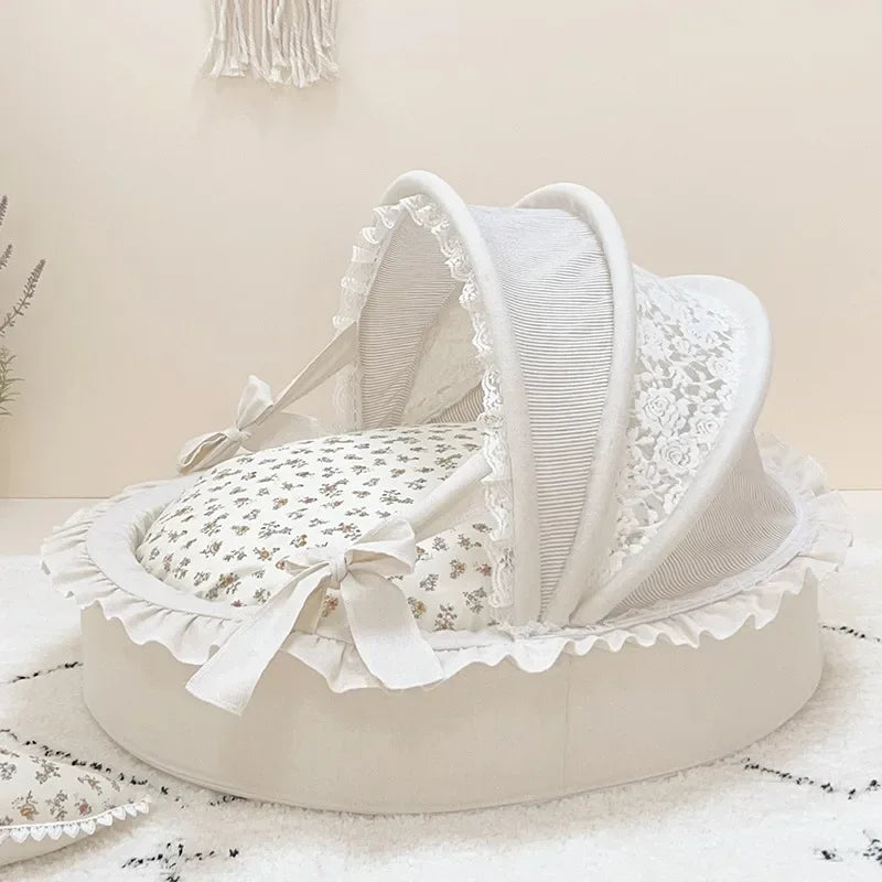 Off-white luxury pet bed with round base, lace-trimmed canopy, ruffles, bows, and floral cushion.