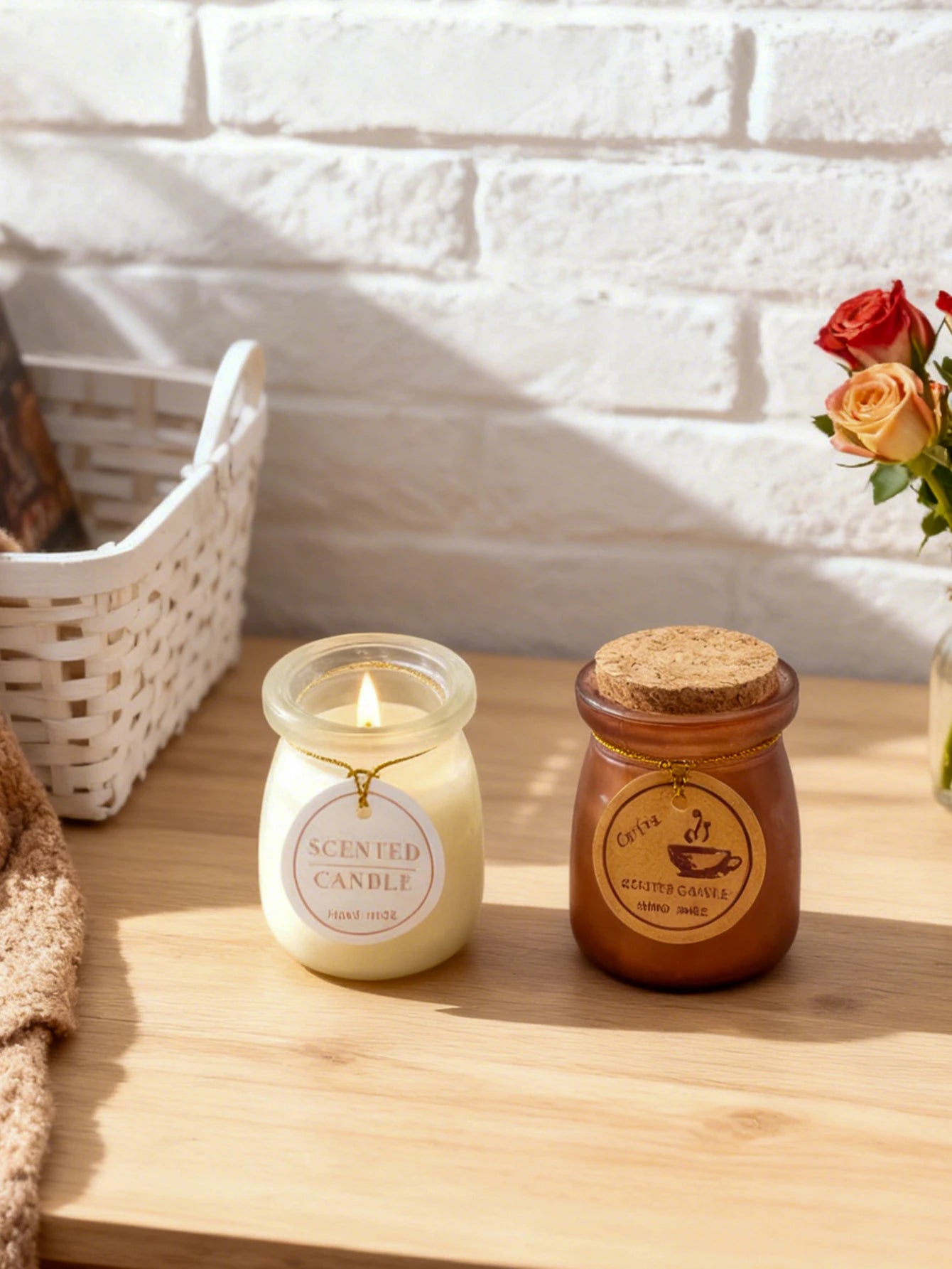 Two scented candles in glass jars: one lit white candle and one amber candle with a cork lid on a wooden surface.