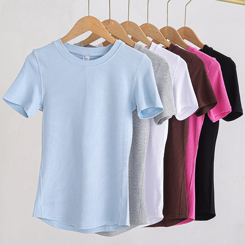 A row of ribbed, short-sleeved crew neck t-shirts hanging on wooden hangers in various colours.