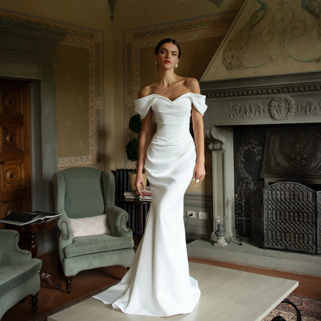 White satin mermaid wedding dress with off-the-shoulder sweetheart neckline and fitted bodice.