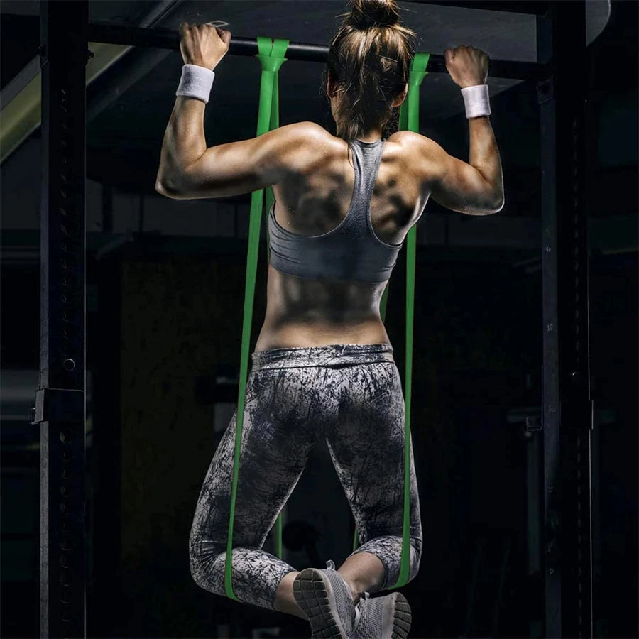 Woman in gym gear doing a pull-up with bright green resistance bands hanging from a black pull-up bar.