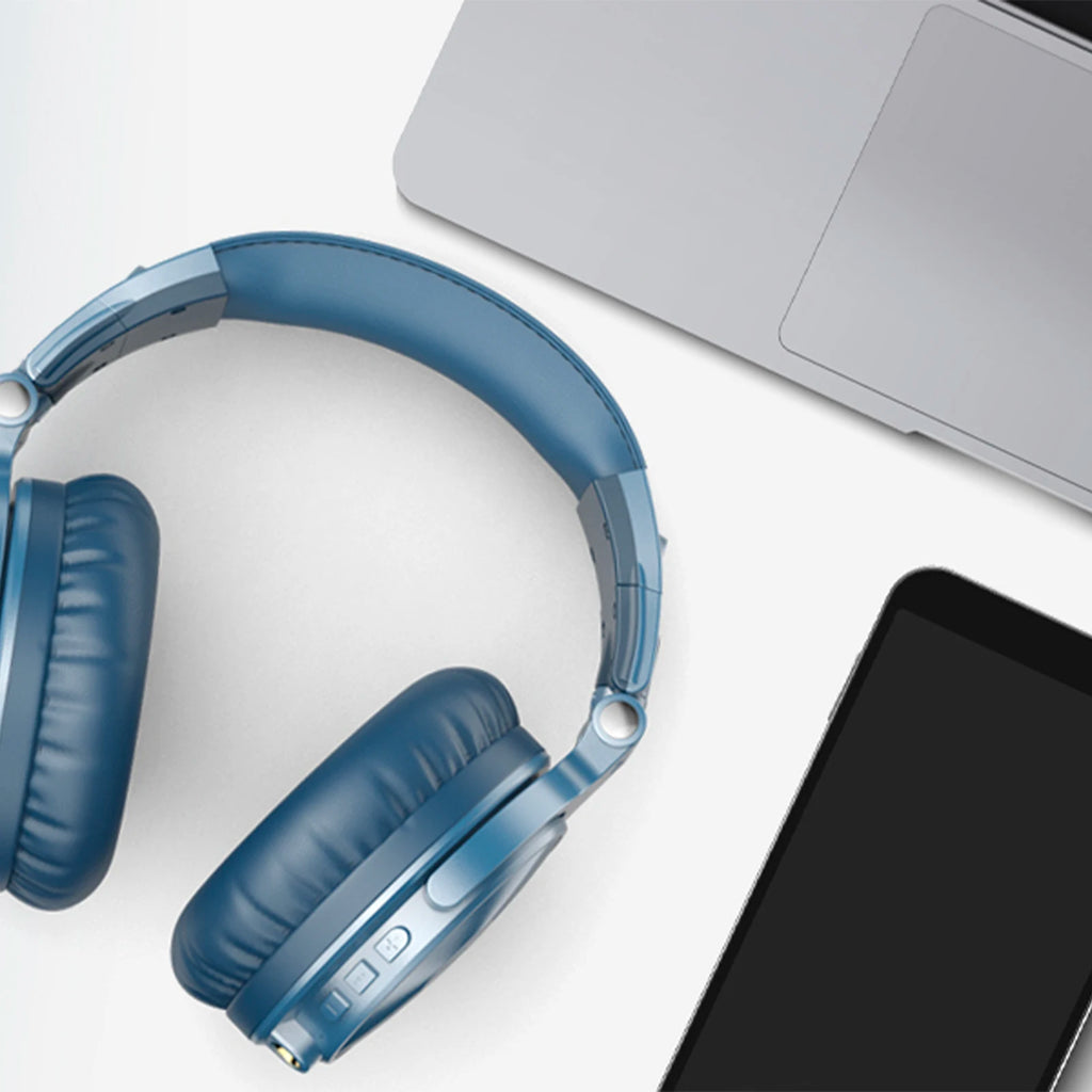 Blue wireless over-ear headphones with cushioned pads, control buttons, and microphone, next to a laptop and phone.