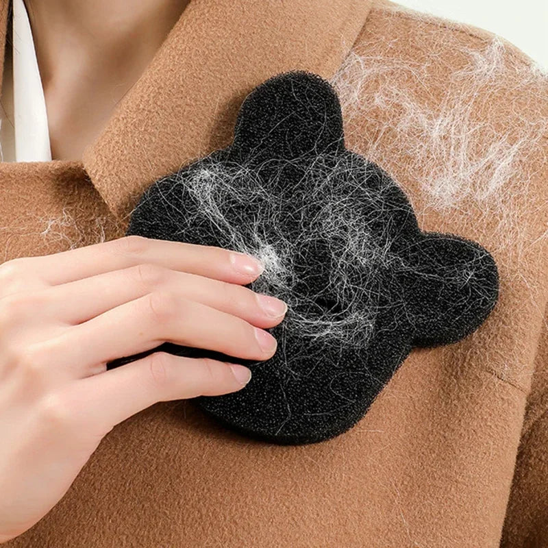 A person uses a black, bear-shaped sponge to remove white lint from a brown coat.