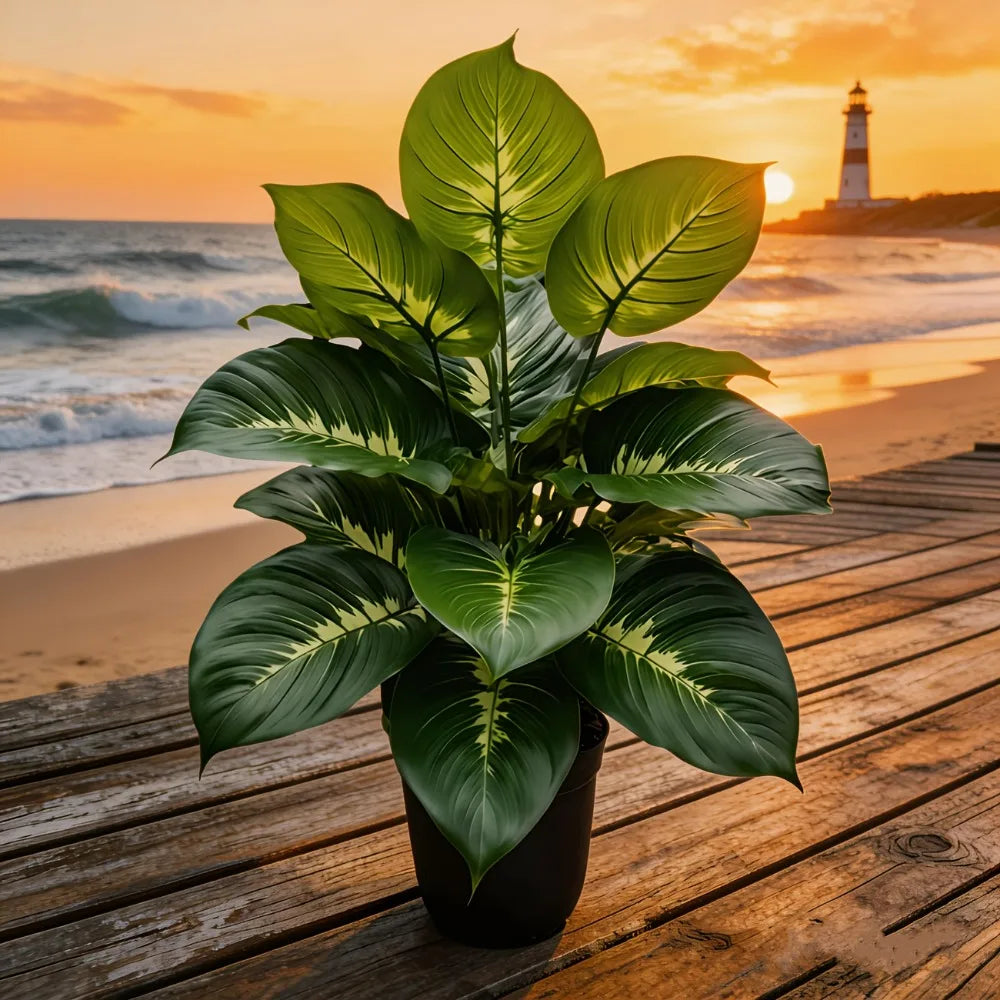 Artificial plant with large, variegated green leaves in a black pot on a wooden pier at sunset with a lighthouse.