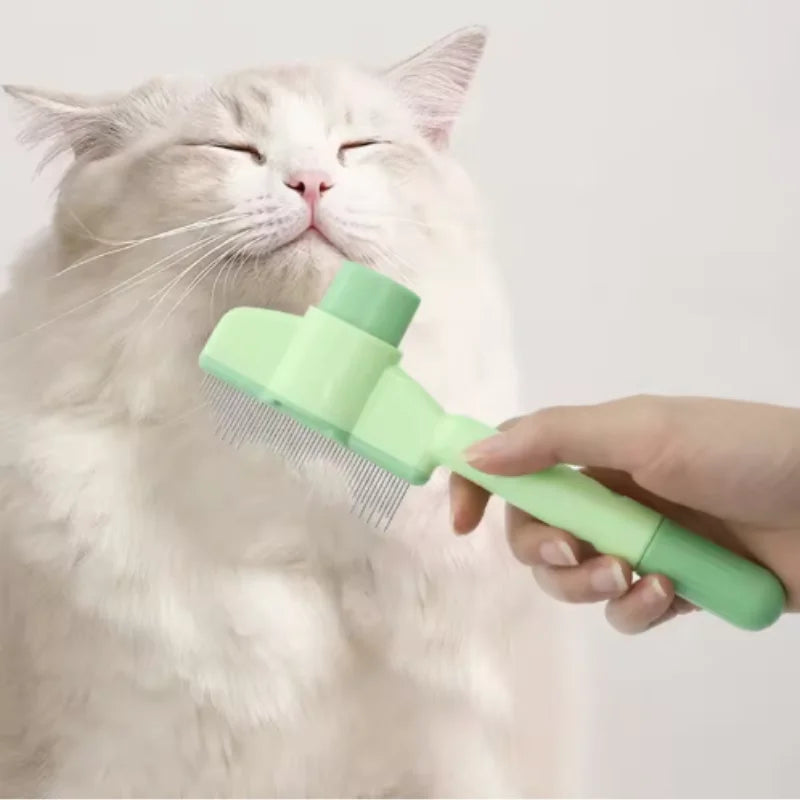 A hand brushes a fluffy white cat with a light green, self-cleaning pet grooming brush with fine metal bristles.