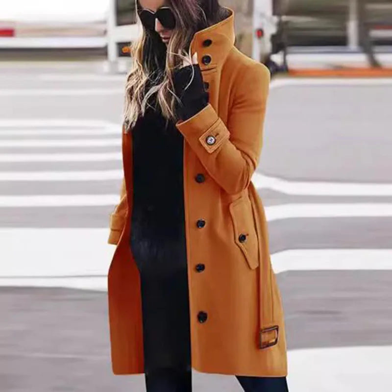 Mustard yellow longline coat with high collar, button front, and buckled cuffs, worn over a black outfit.