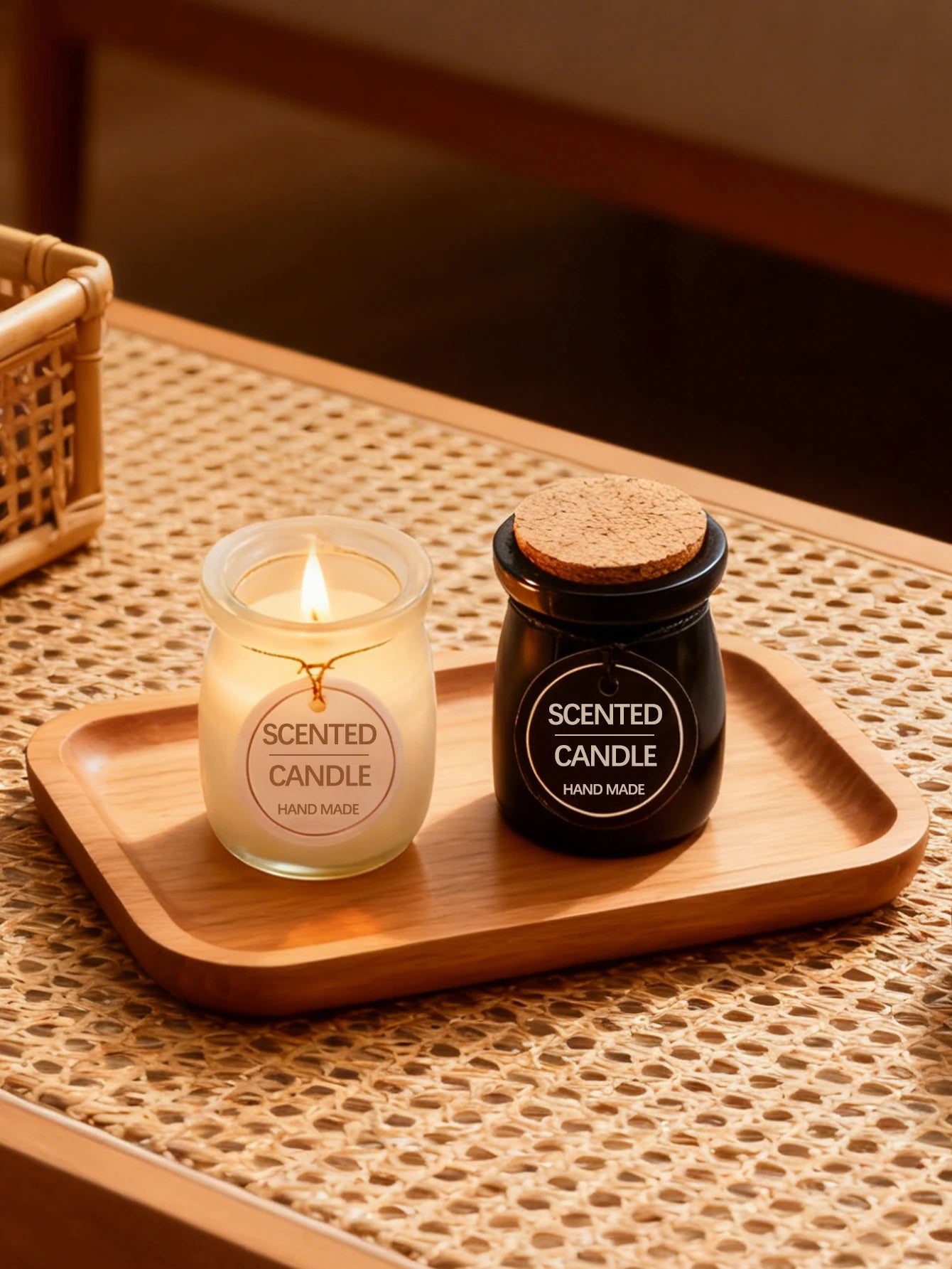 Two handmade scented candles, one clear glass and one black, with cork lids on a wooden tray.