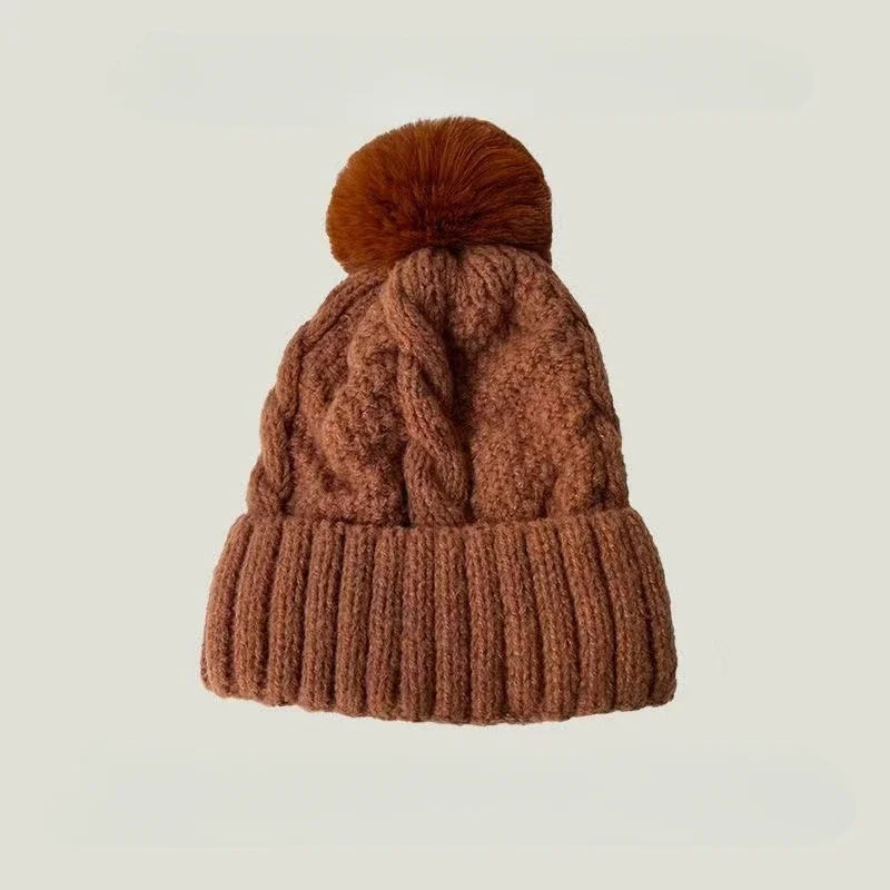 Rust-brown cable knit beanie hat with a matching faux fur pom pom and a ribbed turn-up hem.