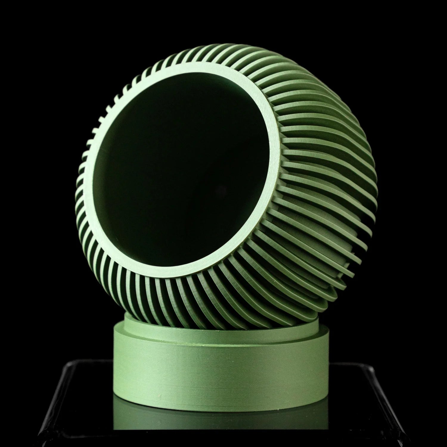 A sage green, 3D-printed planter with a spherical, ribbed design, set on a cylindrical base against a black background.