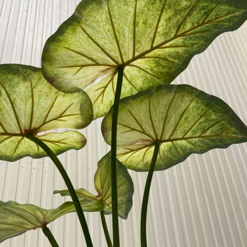 Low-angle view of artificial lotus leaves with green and yellow veined patterns against a white paneled background.