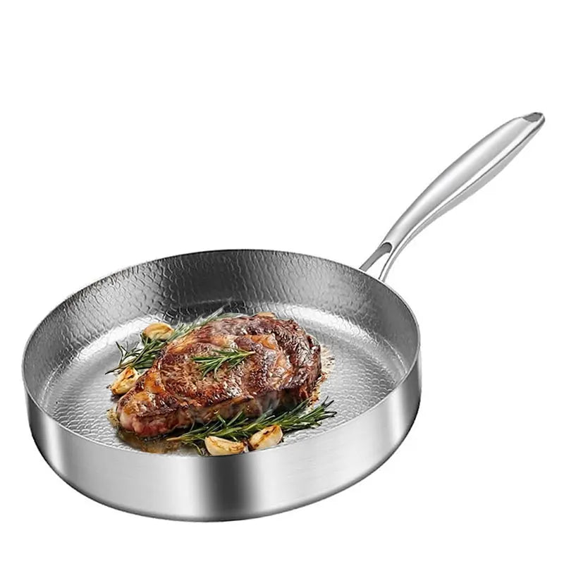 A stainless steel hammered frying pan with a cooked steak, rosemary, and garlic inside.
