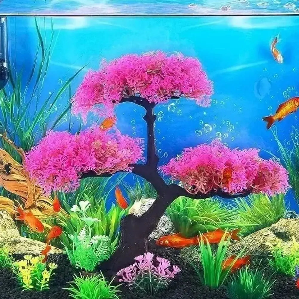 Artificial pink cherry blossom tree decoration inside an aquarium with black gravel, green grass, and goldfish.