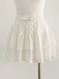 White A-line mini skirt with a smocked elastic waistband, tie-up drawstring, and layered ruffled tiers.