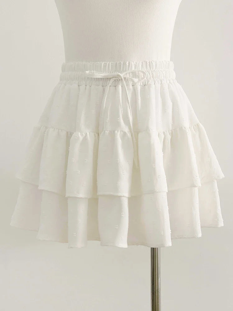 White A-line mini skirt with a smocked elastic waistband, tie-up drawstring, and layered ruffled tiers.