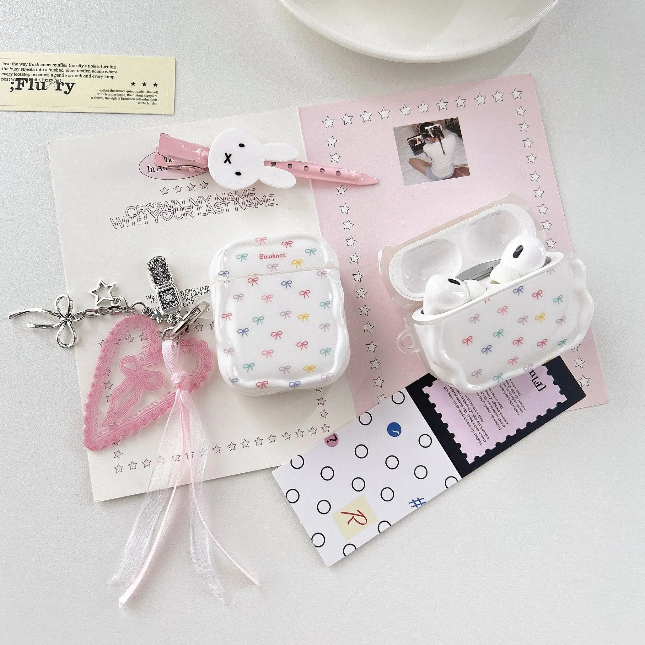 White glossy silicone AirPods case featuring a colourful bow print, complete with a heart-shaped charm accessory.