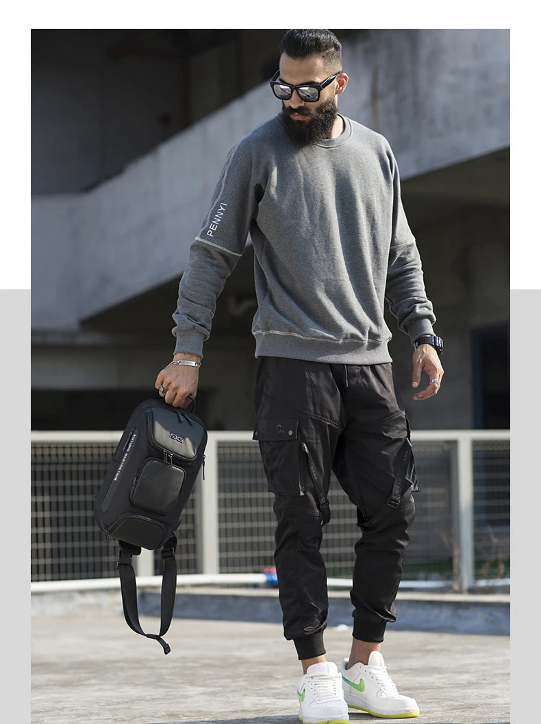A man holds a sleek, black, structured anti-theft crossbody bag with multiple zipped compartments.
