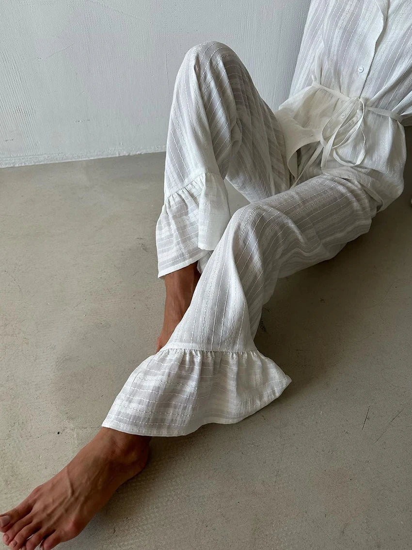 White striped loungewear set with button-down shirt, waist tie, and flared trousers featuring ruffled hem detailing.