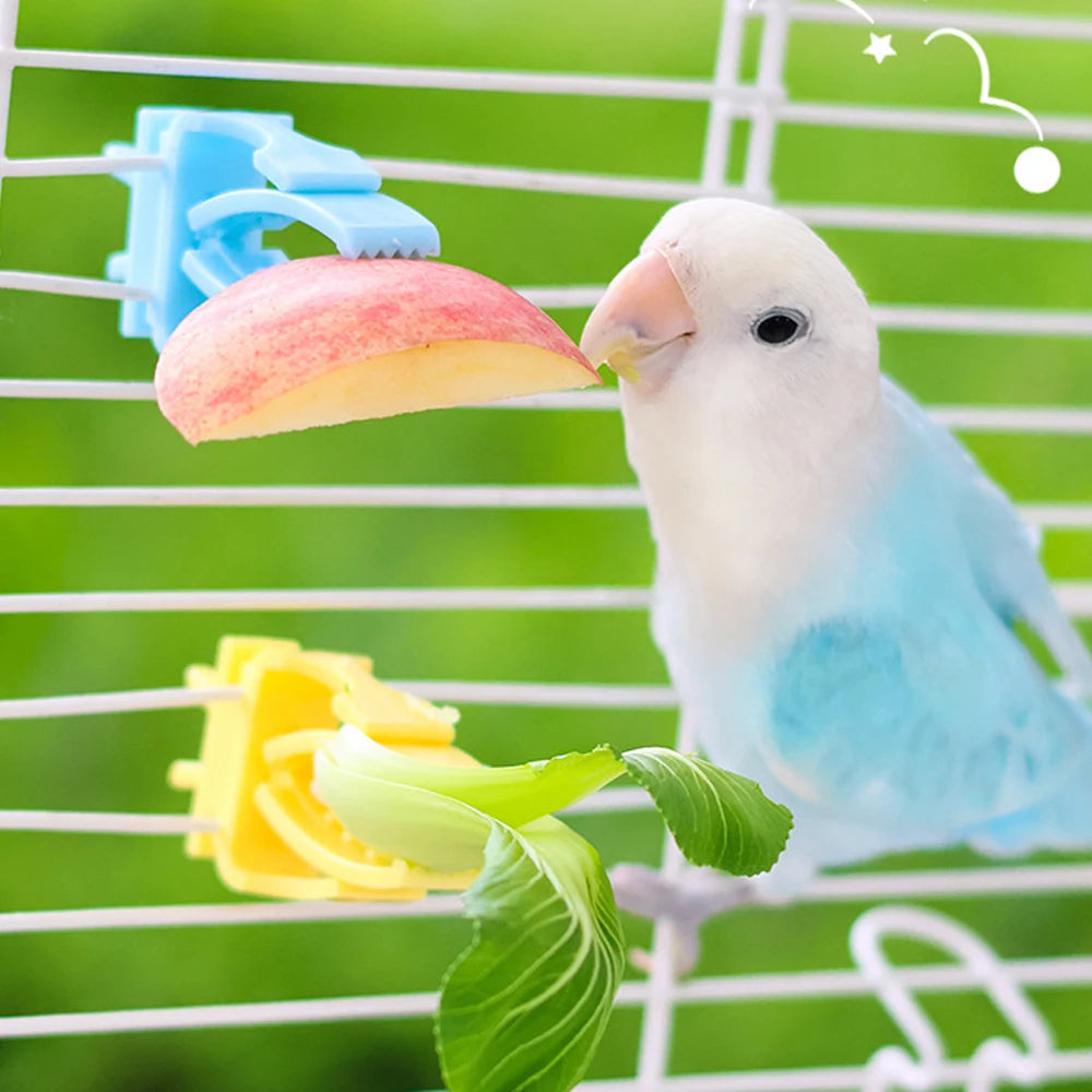 Blue and yellow plastic bird cage food clips holding a slice of apple and greens for a small bird to eat.