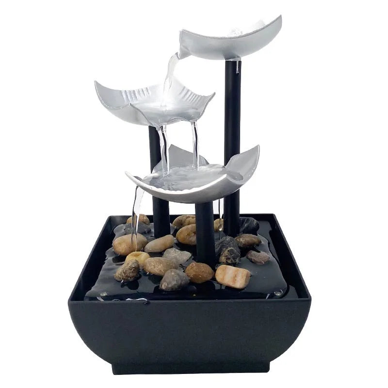 Modern three-tier tabletop water fountain with silver scalloped bowls, black pillars, and decorative river stones.