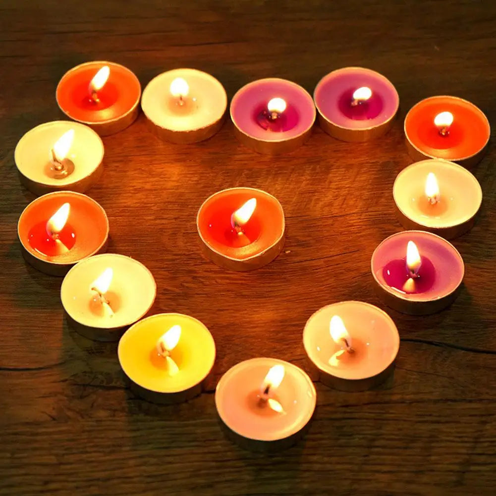 Lit tea light candles in vibrant colours arranged in a heart shape on a rustic dark wooden surface.