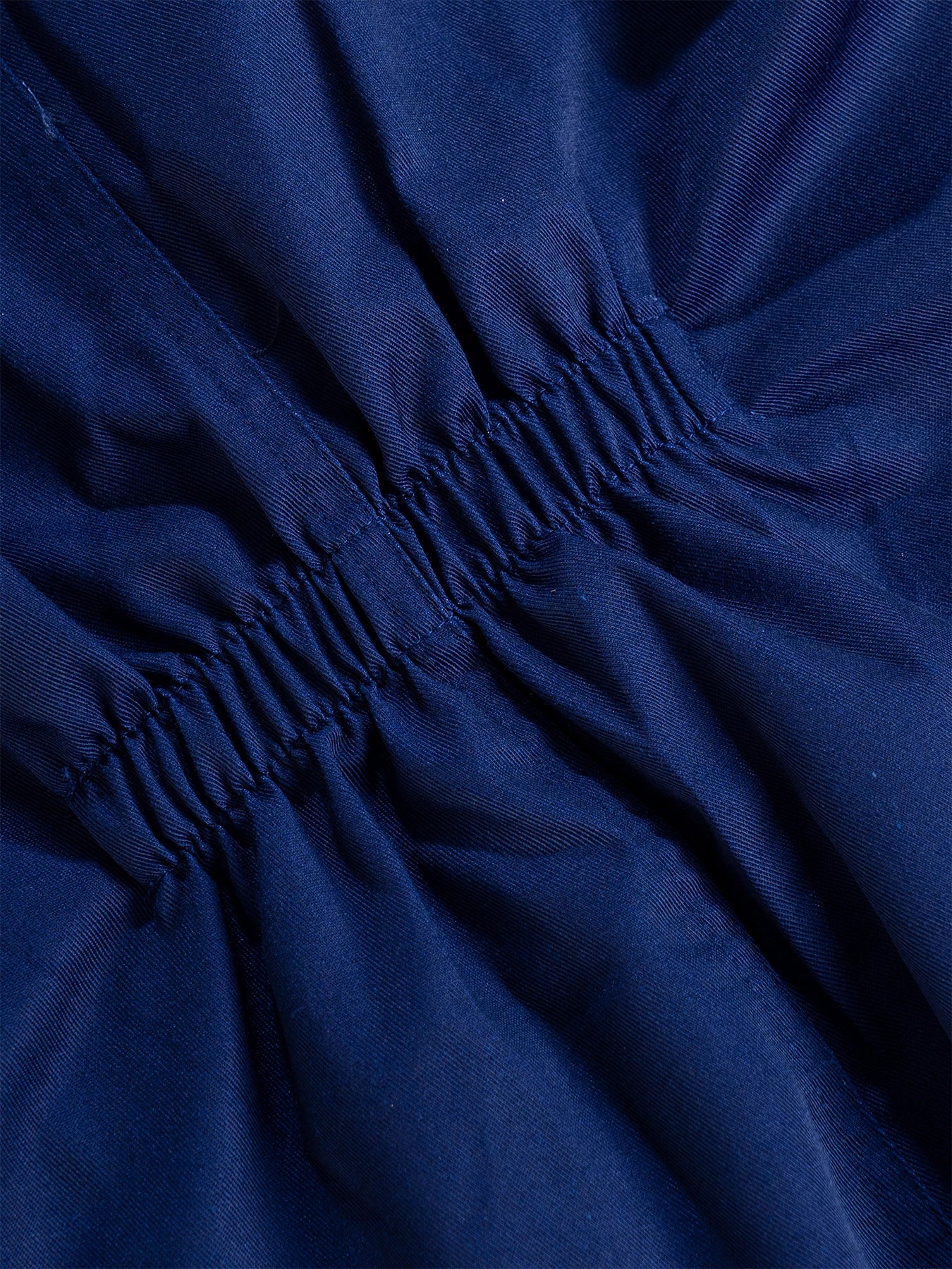 Close-up of navy blue durable fabric on bib overalls, highlighting the gathered, elasticated waist detail.