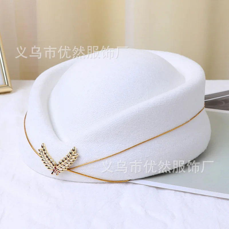 White vintage-style pillbox stewardess hat with a gold trim and leaf-shaped emblem on the front.
