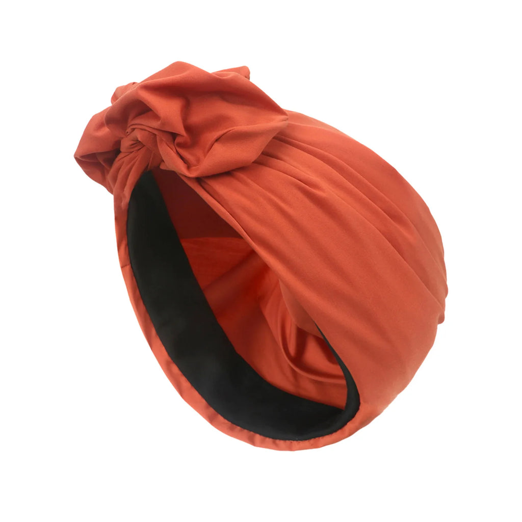 Rust-coloured vintage style knotted turban hat with a contrasting black inner lining.