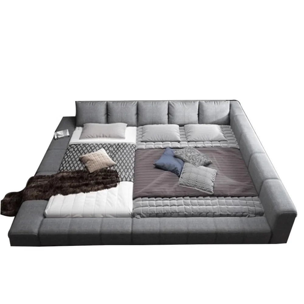 Modern, large grey fabric double bed with a cushioned surround and padded headboard, styled with various cushions.