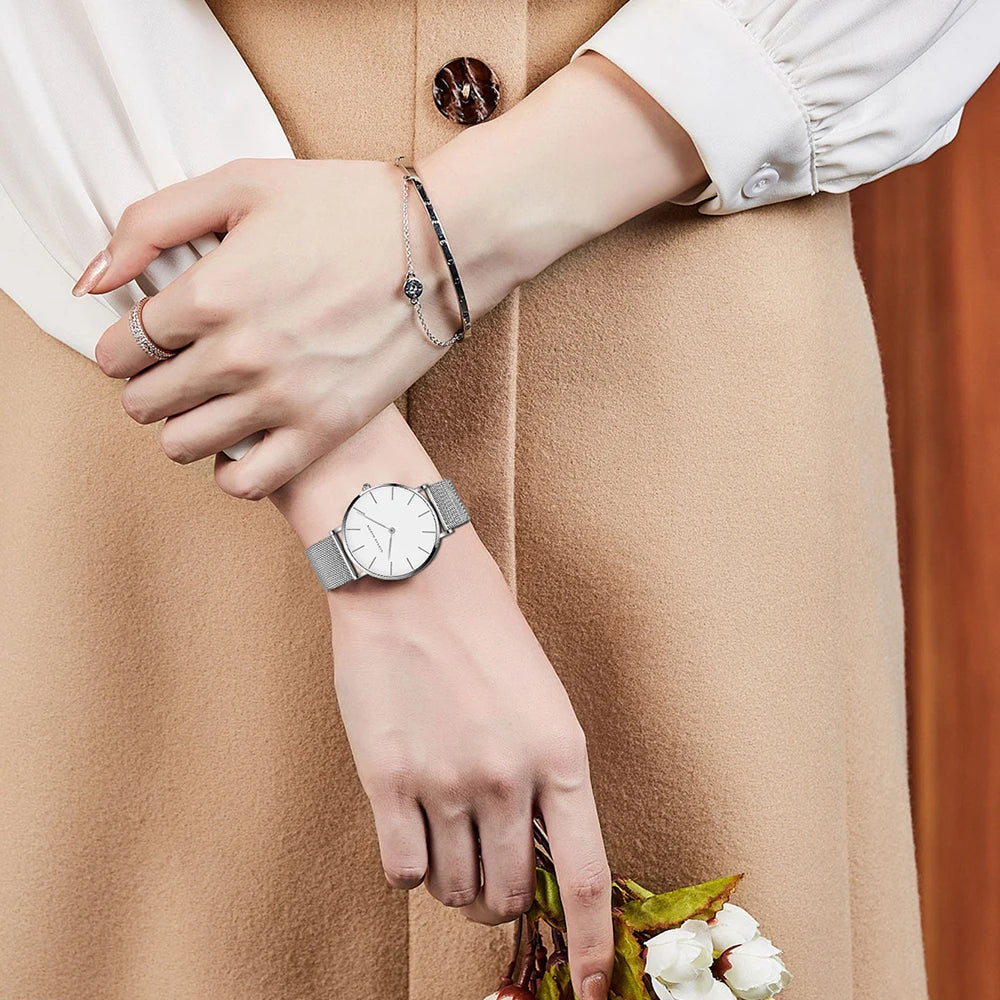 Minimalist silver women's watch with a round white dial and mesh strap worn on a wrist.