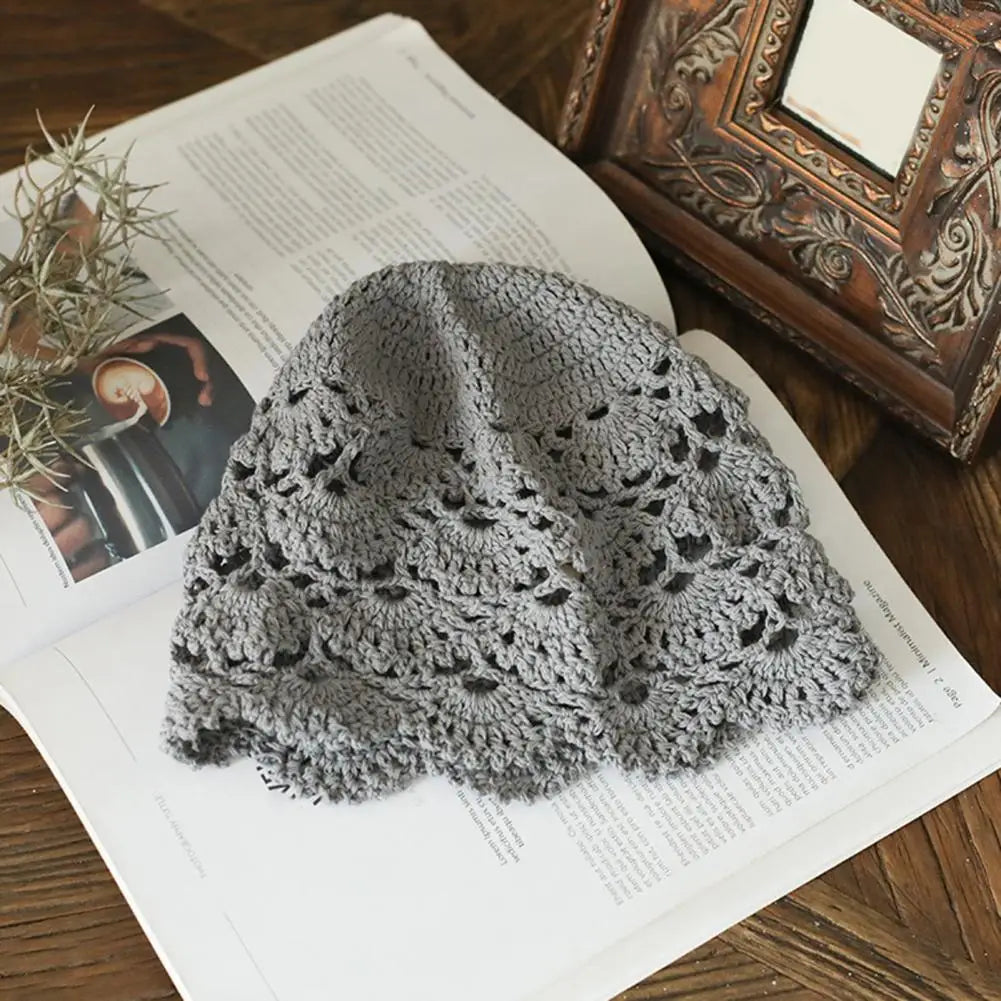 Grey hollow crochet lace beanie hat with an intricate floral pattern, resting on an open magazine.