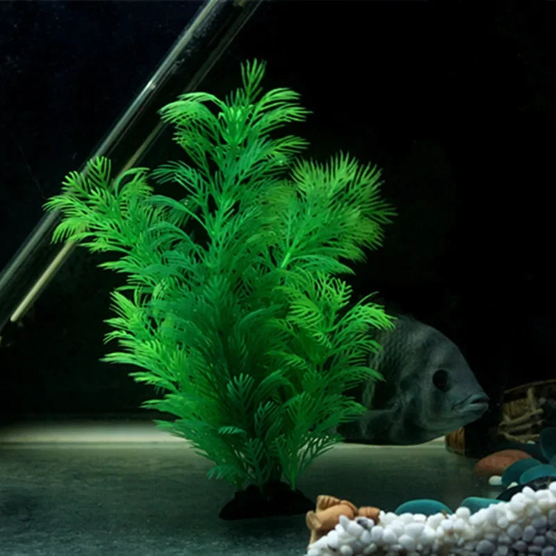 Bright green artificial aquatic plant with feathery, needle-like foliage in a dark fish tank with a grey fish.