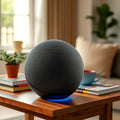 A spherical, dark grey fabric-covered Bluetooth speaker with a glowing blue RGB light base on a wooden table.