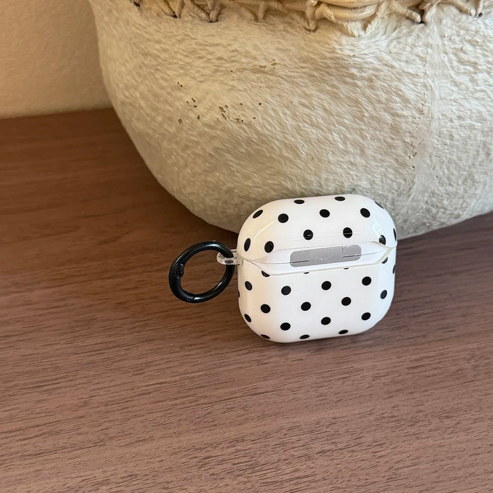 White AirPods case with black polka dots, made of glossy plastic with a black carabiner clip.