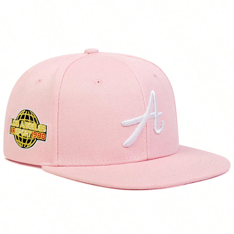 Light pink baseball cap featuring a white gothic 'A' on the front and a globe-themed embroidered patch on the side.