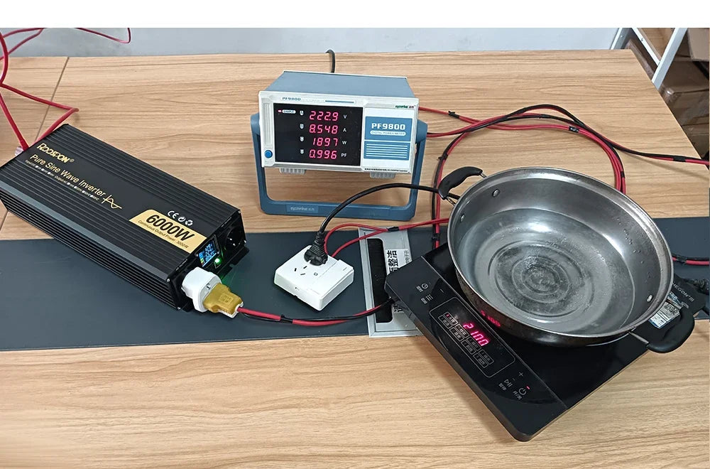 Black 6000W power inverter connected to a digital meter and an electric hob heating a pot of water on a desk.