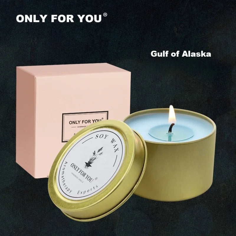 A lit soy wax candle in a gold metal tin, featuring blue wax and a pastel pink gift box.
