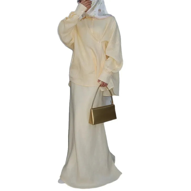 Cream button-down shirt and matching long, flowing skirt set with a structured gold handbag.