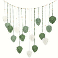 Boho macrame wall hanging featuring sage green and cream leaf motifs on a string with decorative wooden beads.